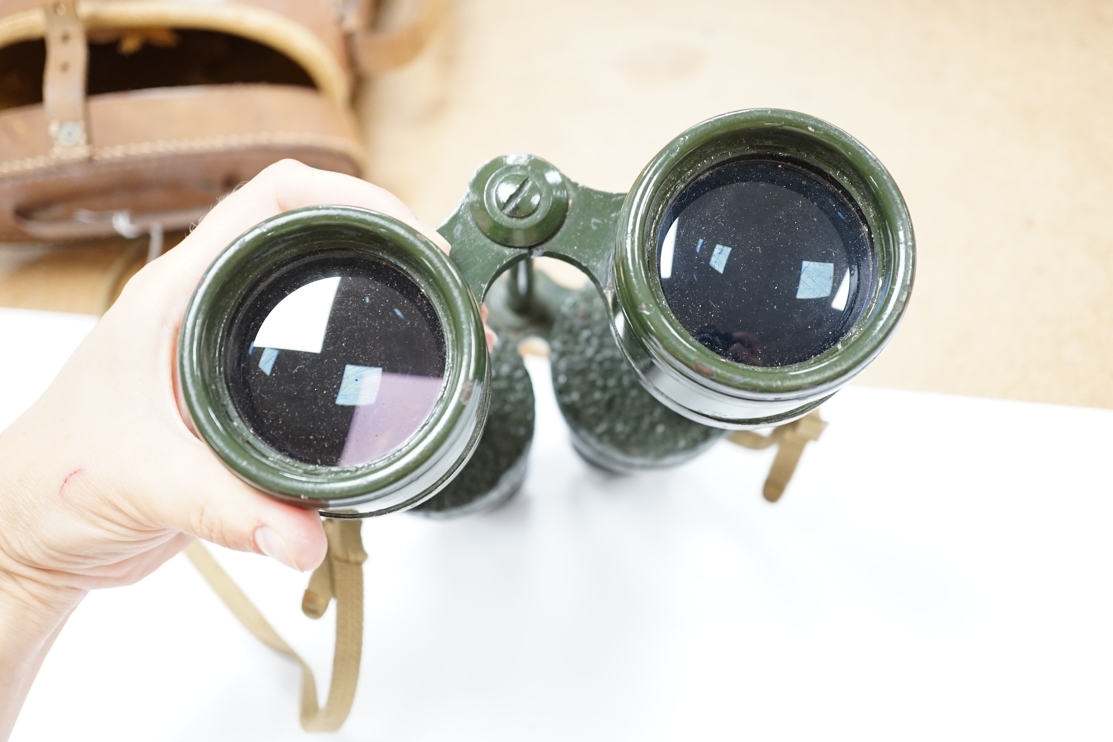 A pair of leather cased, green painted military Binoprism No.5 Mk.4 binoculars, dated 1943, the lid of the leather case impressed with; ‘ 1945 OS/997 Binocular Prismatic No.5 case Mk.1.’ Condition - fair to good, some an